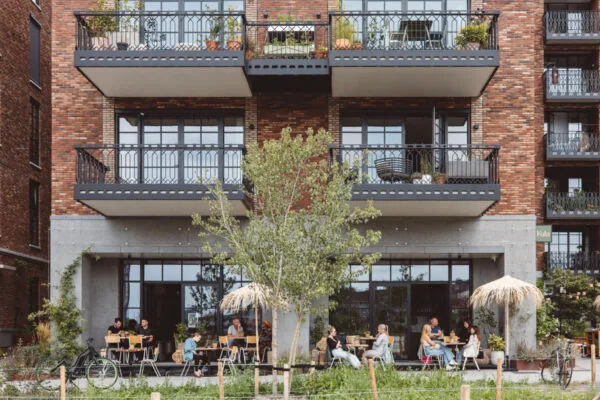 Terras met mensen voor een modern appartementencomplex aan de Karl Weisbardstraat.